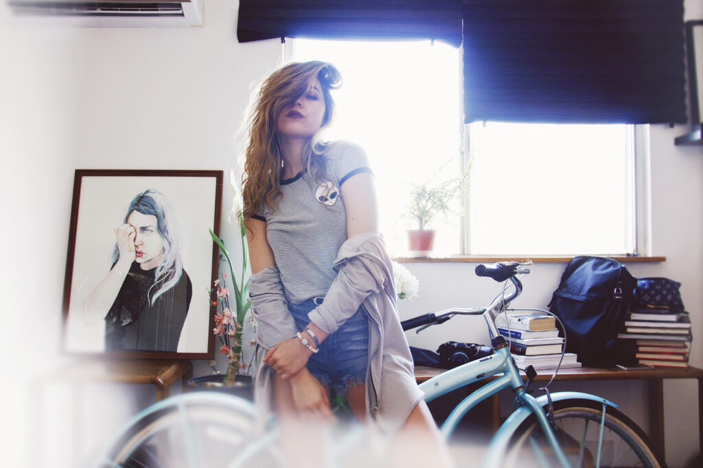 Darian Rojas poses in a sunlit room with a bicycle books and artwork.